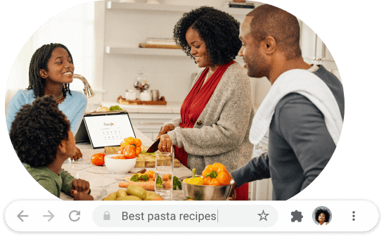 Two adults and two children are gathered in a kitchen chopping vegetables. A laptop is open with Google search displayed.