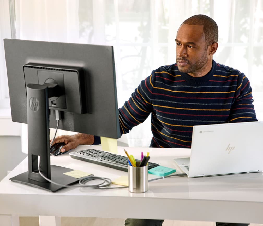Iemand met een gestreept shirt zit aan een bureau en werkt op een Chromebook die is aangesloten op een externe monitor.