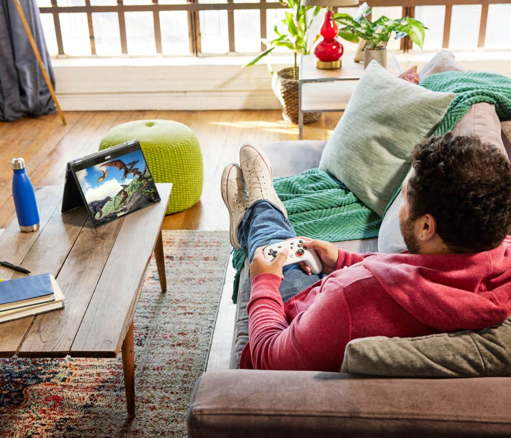 Iemand zit languit op de bank en speelt videogames op een Chromebook met een gamecontroller.