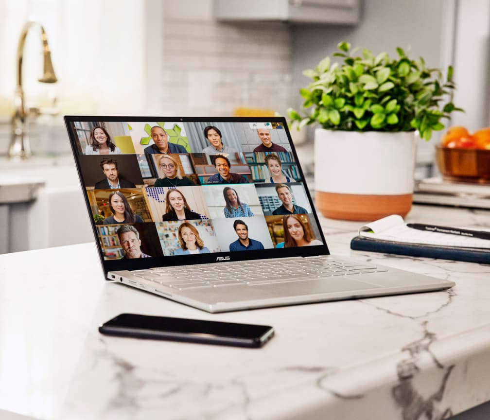 Een geopende Chromebook op een wit marmeren keukenblad met een mobiele telefoon aan de linkerkant en een plant op de achtergrond.